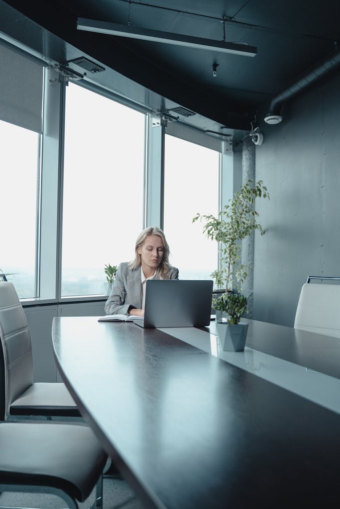 A professional businesswoman working on a laptop in a modern office setting.