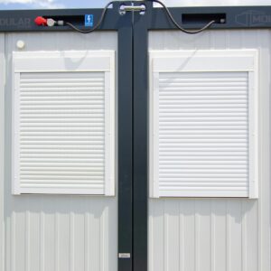 Close-up of a modular building with white shuttered windows and security features under a bright sky.