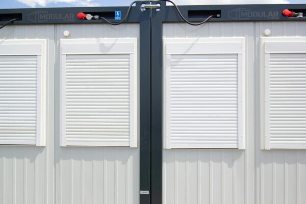 Close-up of a modular building with white shuttered windows and security features under a bright sky.